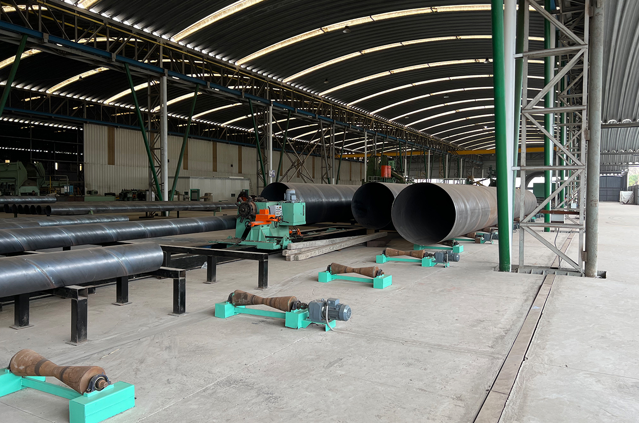Steel pipe sections and fabrication machinery inside an industrial workshop
